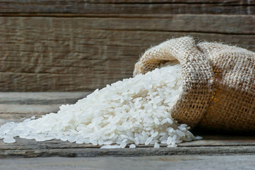 turkish raw white rice grains in burlap sack on wooden background, healthy food uncooked legumes concept
