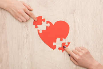 cropped view of women pointing with fingers to pieces of puzzle and paper heart
