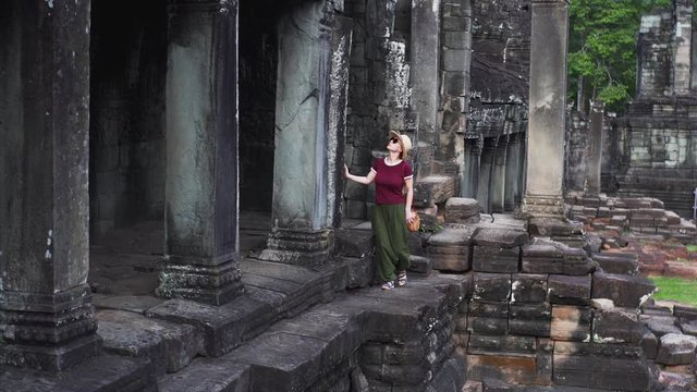 Young woman in hat is walking on ruins of Bayon Temple, a Khmer temple at Angkor in Cambodia built in the late 12th or early 13th century and richly decorated