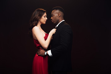 beautiful woman in red dress posing with african american man in suit isolated on black with copy space