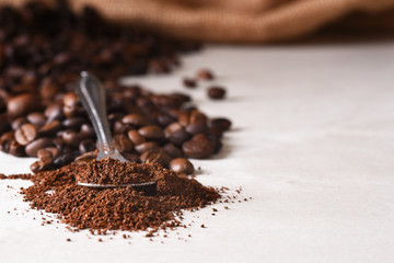 Closeup of a spoonful of coffee grounds with whoel beans spilling out of a burlap sack
