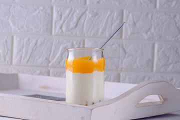 homemade granola in a jar with yogurt and mango mousse in a glass jar on a wooden tray.