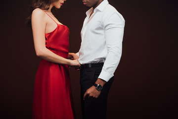 cropped view of woman in red dress undressing african american man isolated on black