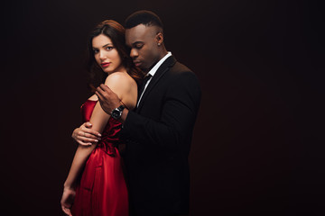 african american man undressing beautiful woman in red dress isolated on black with copy space