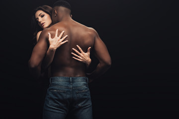 back view of beautiful sexy woman hugging shirtless african american man isolated on black