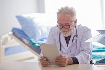 Fototapeta premium Senior doctor using a tablet in patient room.