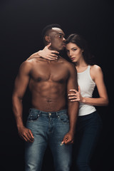 Fototapeta na wymiar beautiful seductive woman embracing shirtless african american man and looking at camera isolated on black