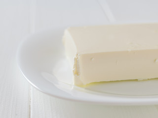 A large piece of cheese on a white plate on a white table. The view from the top. Dairy product.
