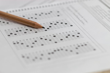 Standardized test exam multiple carbon paper form with gray black answers sheet bubbled and pencil resting on university classroom. Examination knowledge in school concept