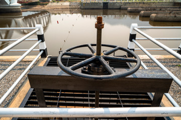 Close-up of black metal cogwheel controlling floodgate with texts in Thai language meaning 