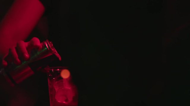 Close-up of professional barman making alcohol cocktail with red bull and ice cubes on the bar counter. Red background.