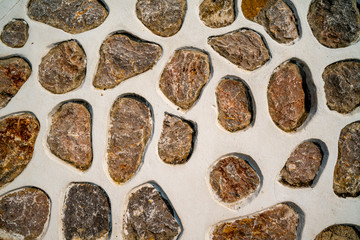 Pattern of brown and gray paving stones decorated on white concrete wall with rough texture.