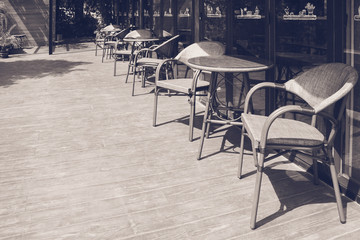 Abstract Black and White image of row of table and chair place on wooden terrace outside of restaurant or coffee cafe.