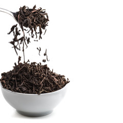 Dried tea pour from the spoon in ceramic cup over white background.
