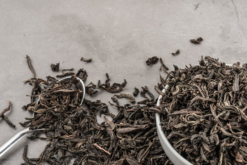 Dried tea in a white ceramic cup with a spoon on a gray textured background.