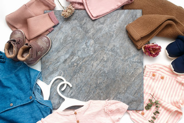 Little lady trendy fashion clothes collage on white, flat lay, top view. Slab of gray marble in a frame of stylish natural things. Fashionable pastel muted shades.Copy space.