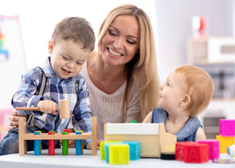 babysitter and children playing together in nursery or day care centre