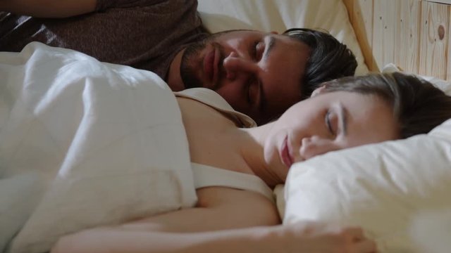Close up view of sensual young couple sleeping in bed together, man wakes up first and kisses his beloved woman. Morning sunshine, couple goals, love, caring. Romantic atmosphere, happy atmosphere