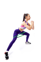 Sporty woman does  exercises on legs, makes lunges  with sport fitness rubber bands  on white background. Photo of muscular woman in sportswear on white background. Strength and motivation.