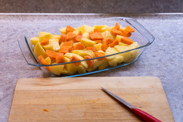 sliced potatoes and carrot in a glass plate, cutting board, knife, kitchen countertop on background, From the side photo