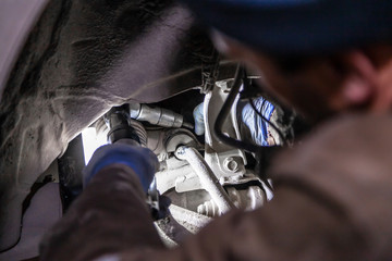 Fototapeta Close up Professional car mechanic makes repairs to the undercarriage of a supported car in auto repair service. Autoworker changes sleeves in garage of repair service station obraz