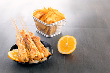 baked fish on skewers in a black plate, french fries and lemon on a wooden table. Copy space