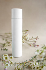 White cosmetic bottle on beige background decorated with white flowers