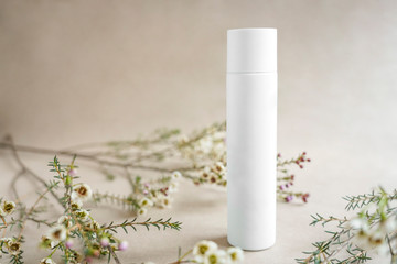 White cosmetic bottle on beige background decorated with white flowers