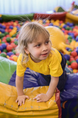 Portrait of a blond boy in a yellow t-shirt. The child smiles and plays in the children's playroom. Ball pool.