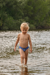 Baby boy barefoot is walking on the beach in water. Child on vacation in summer at the river on good weather.