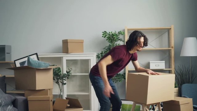 Tired guy is bringing heavy boxes in room suffering from backache touching back with unhappy face during relocation. Sick people and apartments concept.