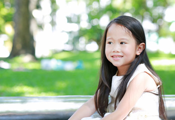 Portrait of smiling little Asian child girl in sunny green park.