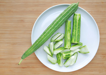 Thai zucchini peeled and sliced on white plate against wooden board background.