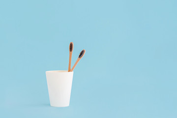 Two wooden toothbrushes in cup on blue background.