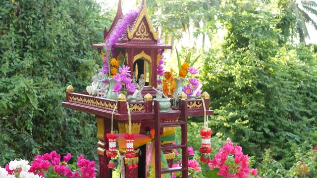 Wooden miniature guardian spirit house. Small buddhist temple shrine, colorful flower garlands. San phra phum erected to bring fortune. Traditional respect animistic rituals, pray ceremonies.