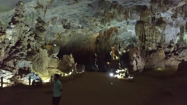 man tourist walks along wonderful spacious illuminated cave with huge stone formations view from flycam