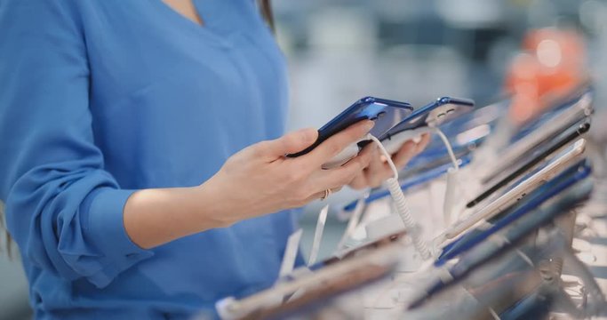 Close-up of a woman holding two new smartphones in her hands and choosing the best phone model in the modern electronics store to buy