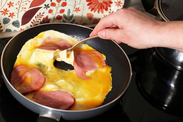 scrambled eggs in a pan with sausage in a black pan, a woman's hand interferes with the scrambled...