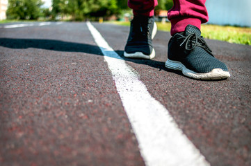 A Child in Sneakers Walks along the White Line at the Running Track on a Summer Day. Making Choice, Crossing Border. Restriction Concept. Copy Space.