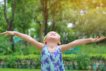 Happy little Asian girl wearing plastic bag (Emergency cap) on head having fun in the summer rain.