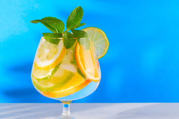 Refreshing cocktail with orange lemon lime mint and ice on a bright blue background