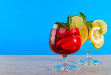 Two refreshing cocktails with orange lemon lime mint and ice on a bright blue background