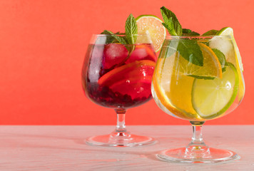 Two refreshing cocktails with orange lemon lime mint and ice on a bright coral background