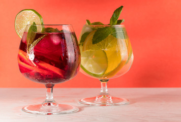 Two refreshing cocktails with orange lemon lime mint and ice on a bright coral background
