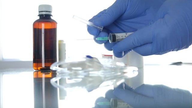 Doctor Hands Protected with Special Gloves Checking a Syringe from the Table