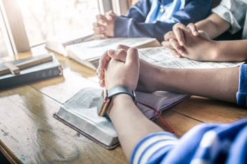 Christian children group praying on wooden table with open bible page at home, prayer meeting concept.