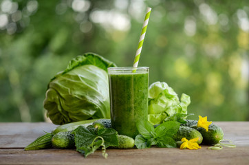  glass with green smoothie on a wooden table and  vegetables with mint leaves