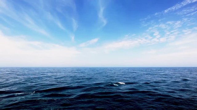 Footage of Calm ocean going by with the beautiful blue streaky clouds above the horizon in the daytime