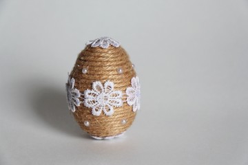 Handmade Easter egg made of twine and lace white flowers on a gray background. Easter theme.