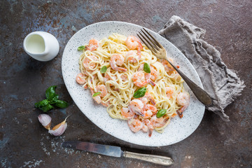 Italian pasta spaghetti in a creamy sauce with shrimp in a plate, top view